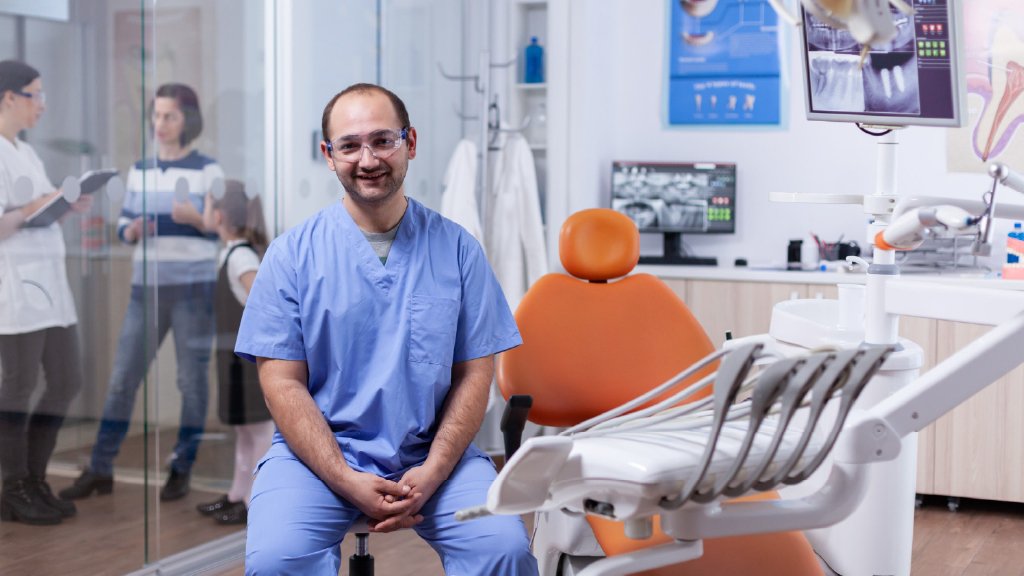 A smiling dentist seated inside a clean, modern dental clinic, creating a calm and welcoming environment for patients